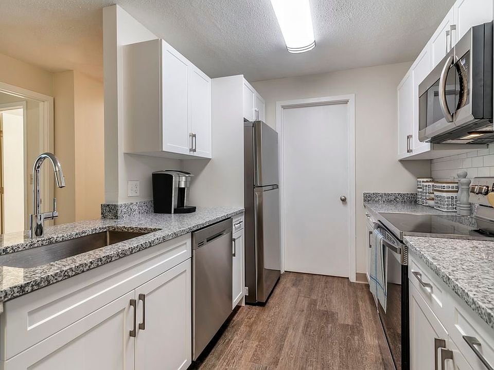 Renovated Package I kitchen with stainless steel appliances, grey speckled granite countertops, white cabinetry, white tile backsplash, and hard surface flooring