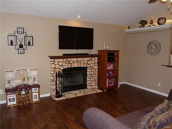 Great room has wide plank laminate flooring, bay window, plant shelving, vaulted ceiling, fireplace & open staircase to finished lower level.