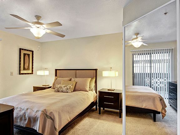 A bedroom with a ceiling fan and mirrored closet