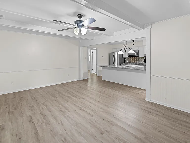 Generous living room with coffered ceiling, ceiling fan, and open view to the fully-equipped kitchen.