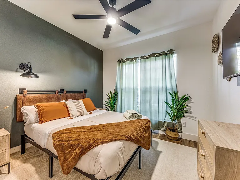 Bedroom featuring a ceiling fan with integrated lighting, a window with light-filtering curtains, and wood-finish flooring
