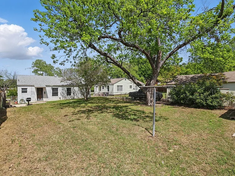 Expansive backyard with a paver patio, established trees providing natural shade, and a storage shed. Grill is non-functioning.