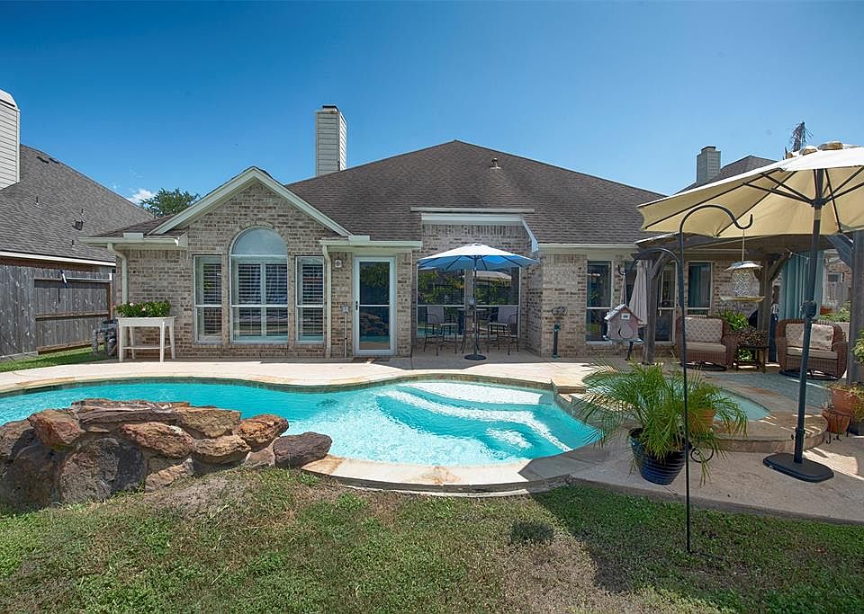 A street view of the home showing the fabulous curb appeal with stone accents surrounding the trees as well as the garden.