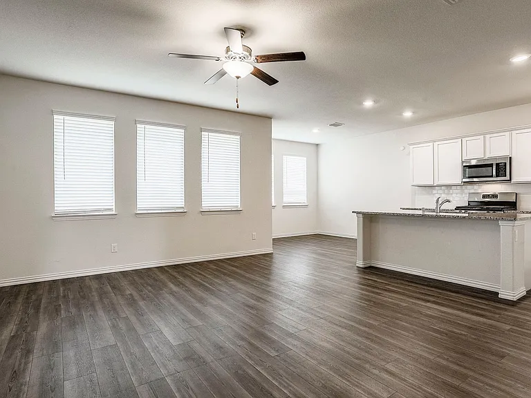 Kitchen featuring dark wood-type flooring, a center island with sink, appliances with stainless steel finishes, stone counters, and white cabinets