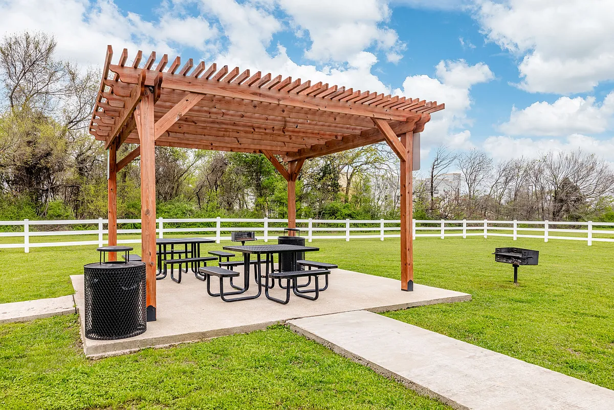 Shaded outdoor picnic area with pergola seating, perfect for relaxing or entertaining - Ambassador Apartments