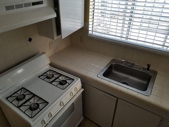 View of the stove, counter, and sink. The walls and counters are tile.