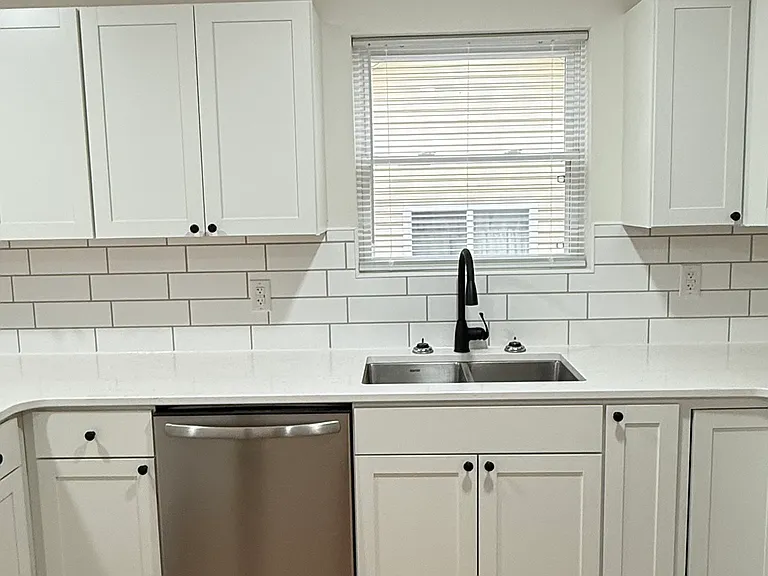 Brand-new kitchen featuring Whirlpool stainless-steel appliances, including range and built-in microwave, modern white cabinetry with ample storage, quartz-style countertops, subway-tile backsplash, and attractive new flooring.