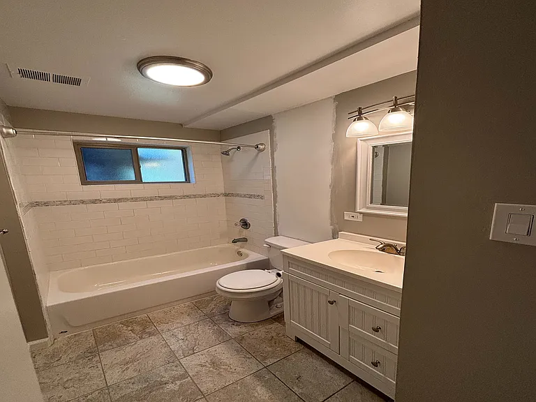 Elegant bathroom with modern lighting, a classic white bathtub, and stylish tile flooring.