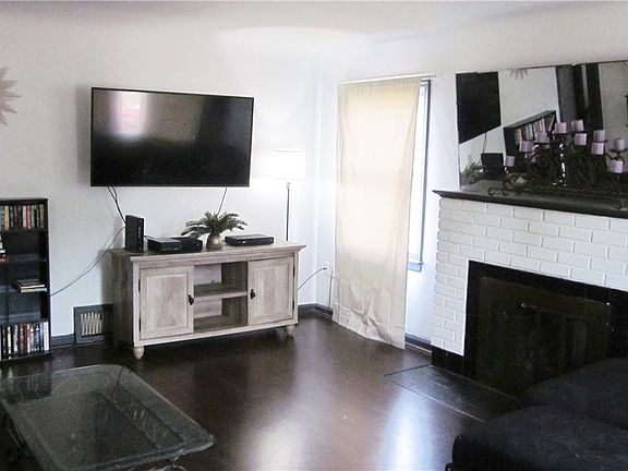 Looking at the Living Room from front door. Large room with a gas fireplace and brick surround, and newer flooring. 