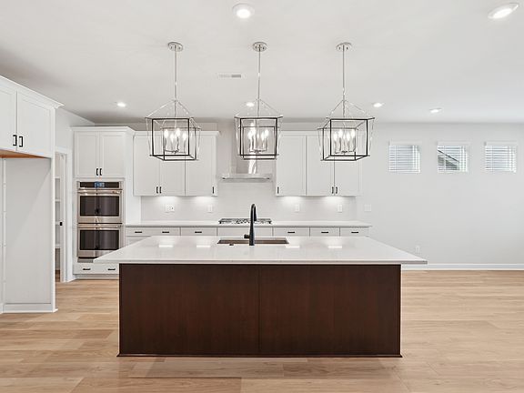 A modern, open-concept kitchen with white cabinets, a dark wood island, and pendant lighting fixture