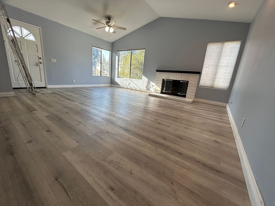 Main room with vaulted ceiling, three windows with garden/street views, ceiling fan, track lighting with individual dimmer controls, cozy gas fireplace.