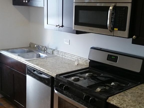 Stainless steel kitchen appliances: dishwasher, microwave, range, refrigerator & stacked washer/dryer machines.