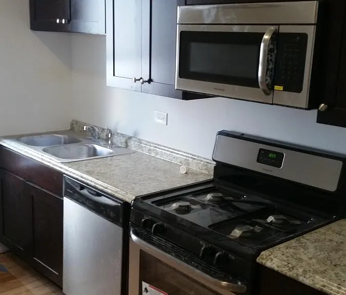 Stainless steel kitchen appliances: dishwasher, microwave, range, refrigerator & stacked washer/dryer machines.