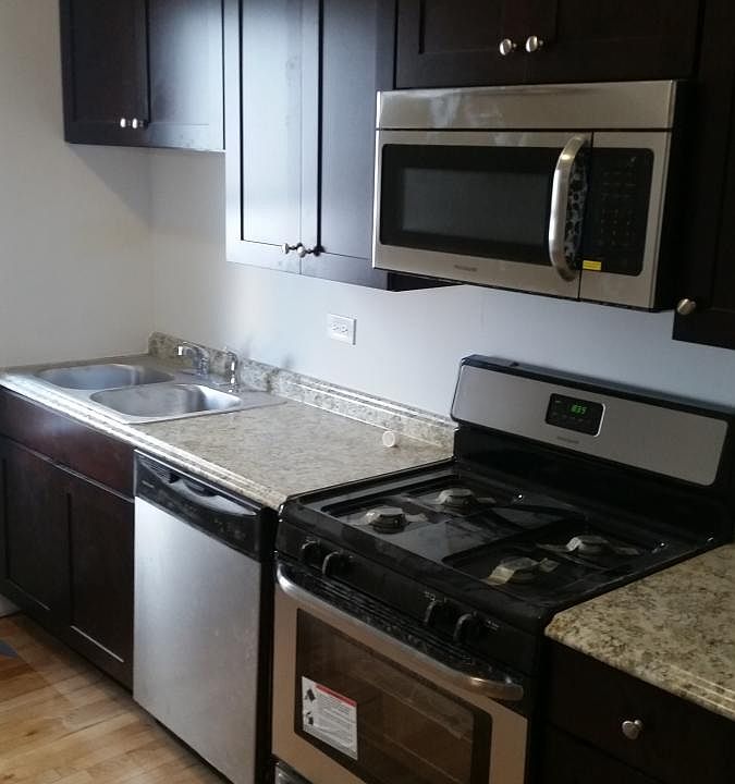 Stainless steel kitchen appliances: dishwasher, microwave, range, refrigerator & stacked washer/dryer machines.