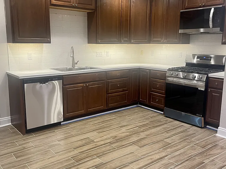 Modern kitchen featuring ample storage, tile backsplash, a brand-new faucet, and all-new appliances, including a refrigerator, dishwasher, gas range, and microwave with ventilation.