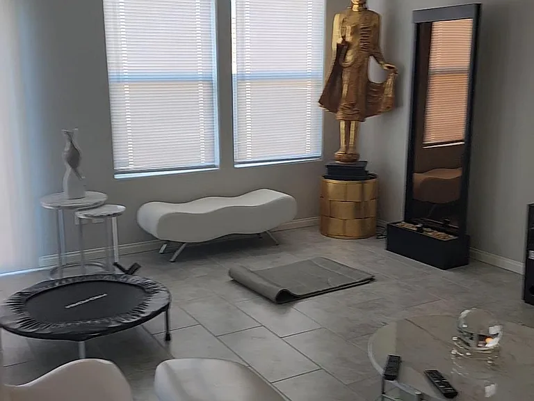 Open living area with tile floors, ceiling fan, and two large windows with blinds, plus flexible space for seating or fitness