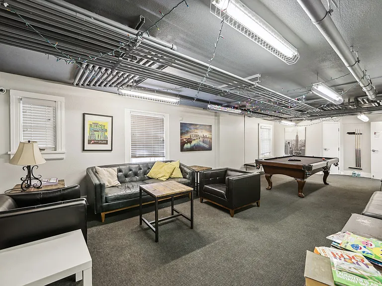 Room with a wooden coffee table surrounded with armchairs, bookshelf, and a flat-screen TV
