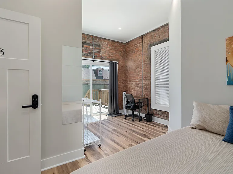 Bedroom with exposed brick accent wall, wood-look flooring, work desk, and sliding door private entrance.