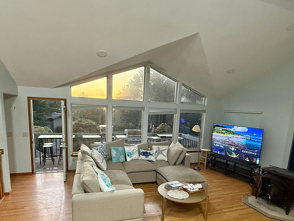 Sun-drenched main living area with soaring vaulted ceilings, cozy fireplace, and panoramic window views showcasing the gorgeous coastal sunset horizon.