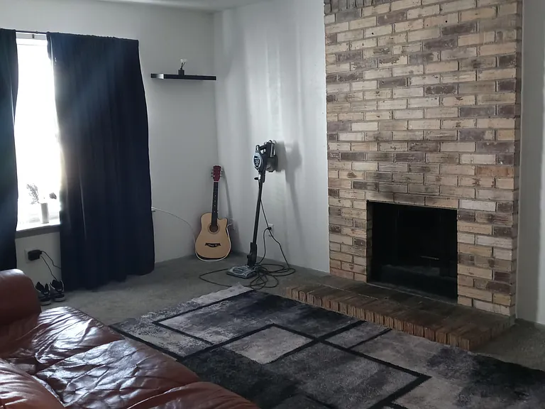Living room with a brick fireplace, comfortable seating area, and a window for natural light and ventilation.