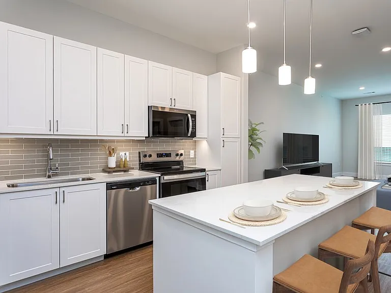 Modern kitchen with white cabinetry, undercabinet lighting, grey tile backsplash, and white quartz countertops
