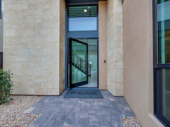 The image shows a modern building entrance with a glass door, stone walls, and a paved walkway leadi