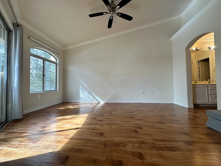 Spacious master bedroom with high ceilings, filled with natural light, and featuring a ceiling fan