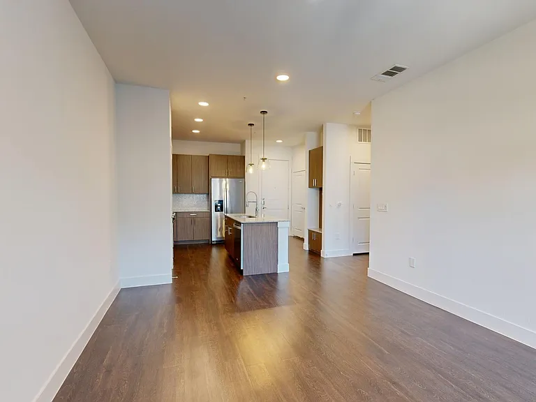 Apartment kitchen with stainless steel appliances, dining and living room with wood-style flooring.