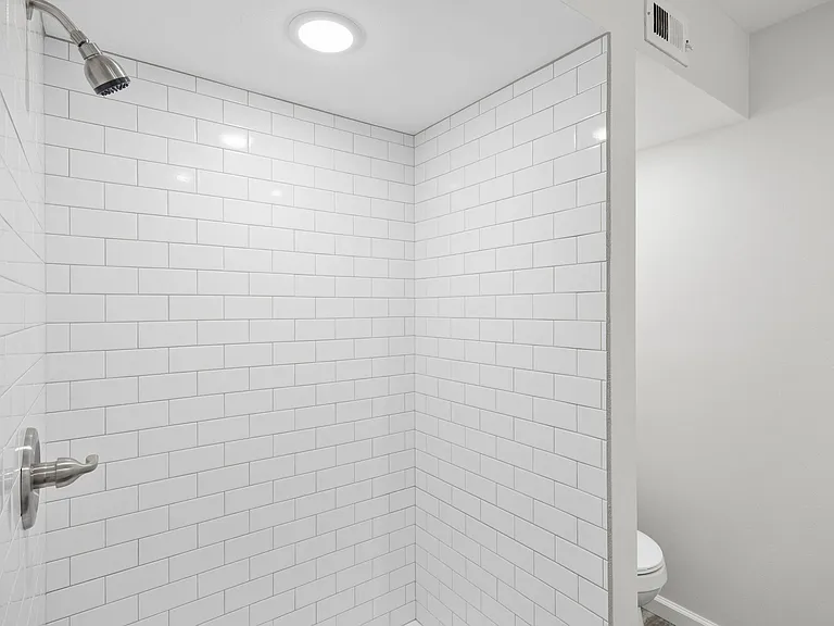Shower enclosure featuring white subway tile, a brushed nickel shower head, and coordinating faucet