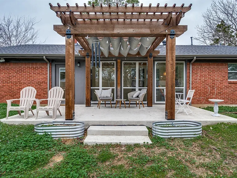 Concrete patio featuring a large wooden pergola with a retractable canopy, a red brick exterior, large glass doors, and two galvanized metal planters