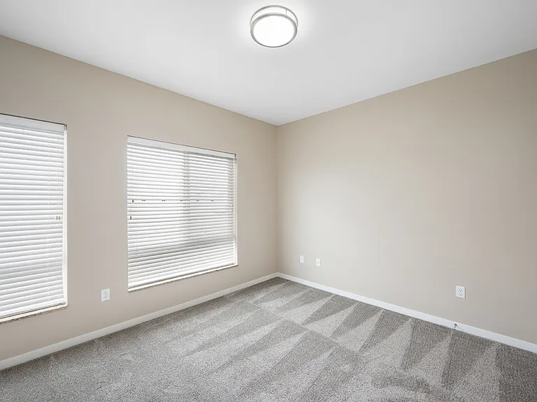 Bright, spacious room with fresh beige walls, plush carpet, and two large windows with blinds. Bright, spacious room with fresh beige walls, plush carpet, and two large windows with blinds.