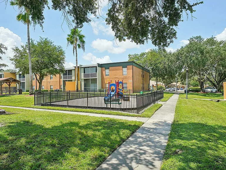 Inviting apartment community with lush green lawns, modern playground, and charming picnic area under open skies.