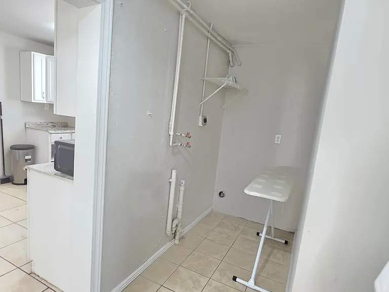 Dedicated laundry nook with washer hookups, utility shelving, and tile flooring located just off the kitchen.