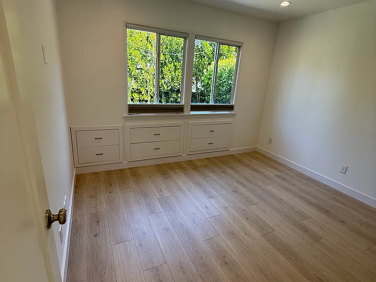 Primary bedroom with built in drawers overlooking private front yard and all new light floors