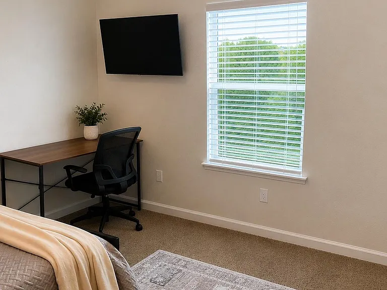 work desk setup, wall-mounted TV, and a large window with blinds.