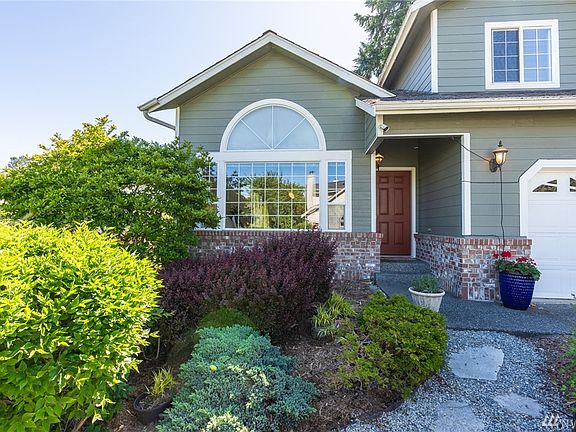 Mature landscaping and brick masonry frames the entry. Drip watering system for potted plants can be removed.