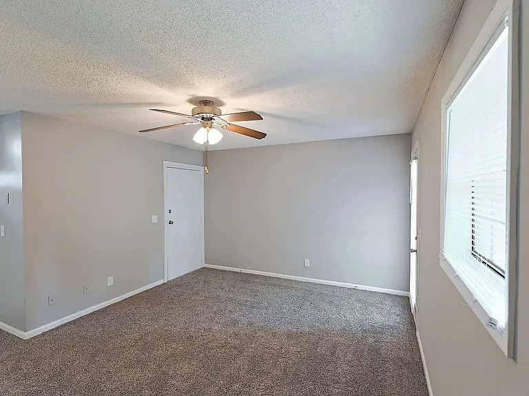 Spacious bedroom with plush carpeting, ceiling fan, and natural light