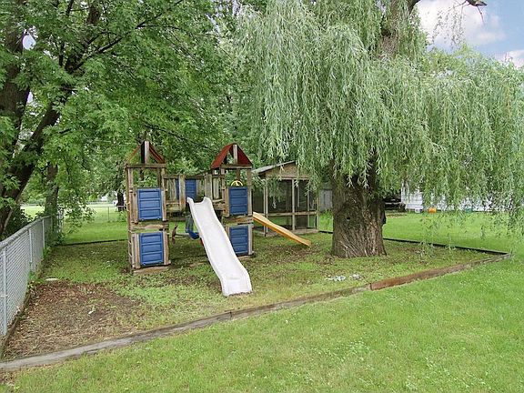 This uncommon back yard is like it's own park, a great place for the kids to play in the shade of mature trees or in the screened sandbox past the slides.
