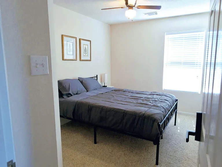 Carpeted bedroom with a ceiling fan, large window with blinds, and space for a full/queen bed plus a nightstand.