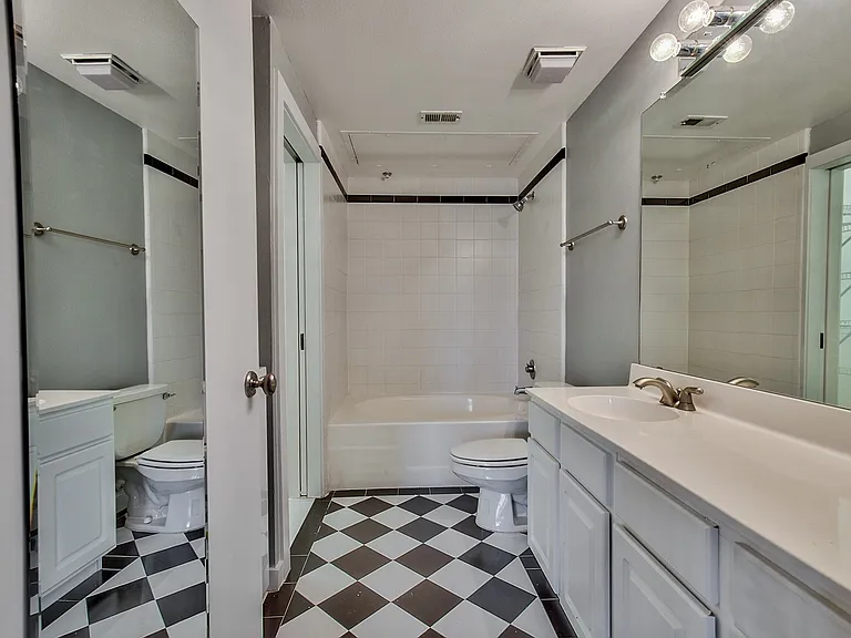 Bathroom featuring checkerboard tile flooring, a white vanity with an integrated sink, and a mirrored wall