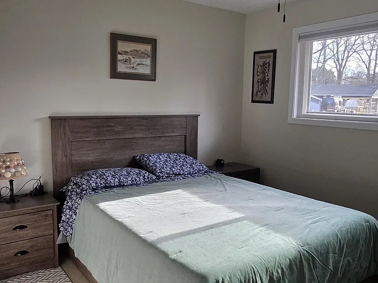 The queen bedroom is furnished with a storage bed, two nightstands, an overhead fan/light, a dresser with a large mirror, and blackout shades.