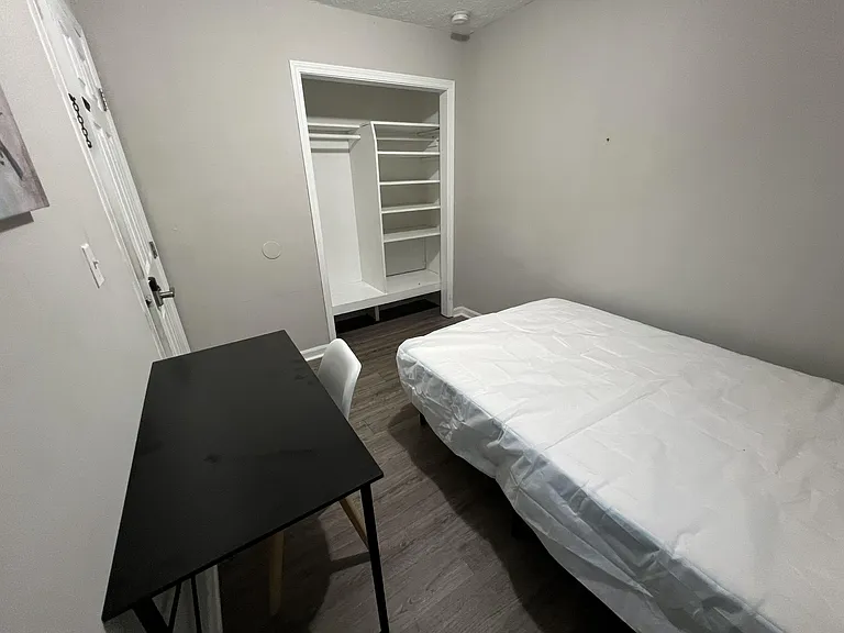 Furnished bedroom with twin bed, desk, and open closet system with shelving for organized storage.
