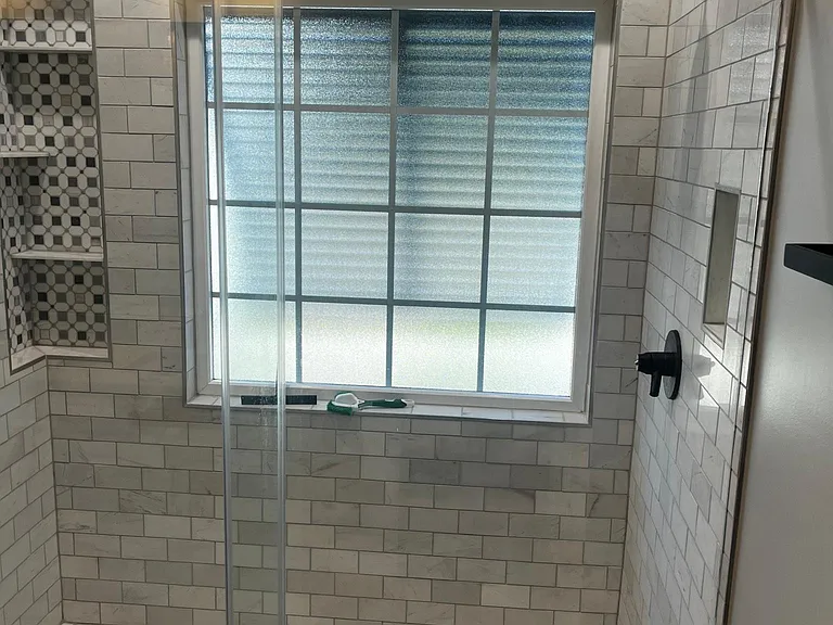 Spacious glass-enclosed shower with a large window, 4 fixtures, and patterned tile floor.