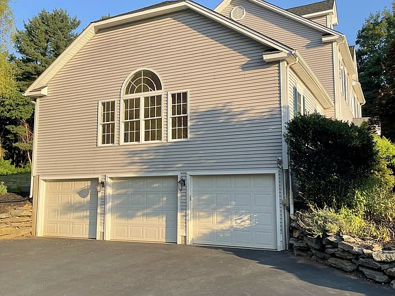 Three-car garage, spacious asphalt area for additional parking, with a basketball hoop