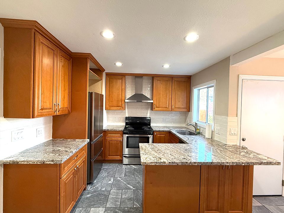Bright and airy updated kitchen with granite countertops, maple cabinets, white subway tile backsplash, stainless steel appliances, bar seating, recessed lighting, ample storage, and slate flooring