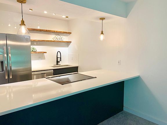 Modern kitchen with quartz countertops, open shelving, stainless appliances and focused lighting