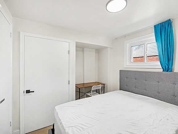 Bedroom with a full bed, upholstered headboard, window with curtains, and a built-in nook featuring a small desk.