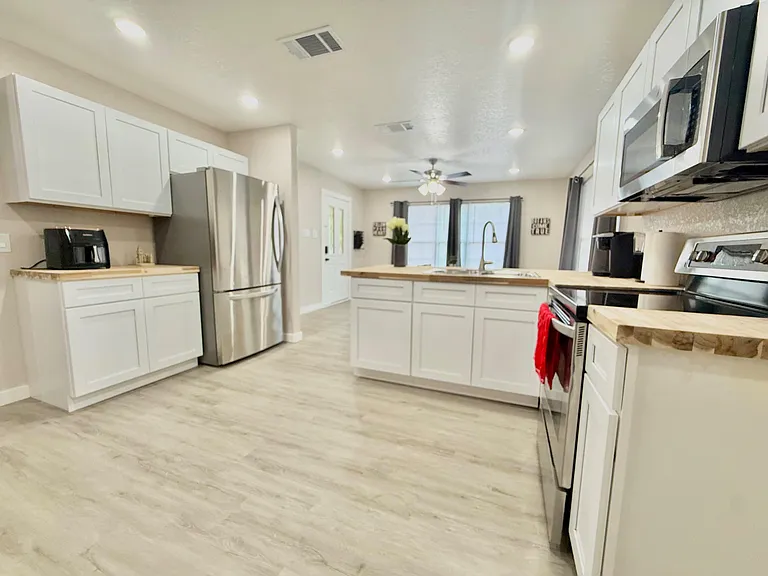 Spacious kitchen with an island sink, shaker cabinets, butcher-block counters, and stainless steel appliances.