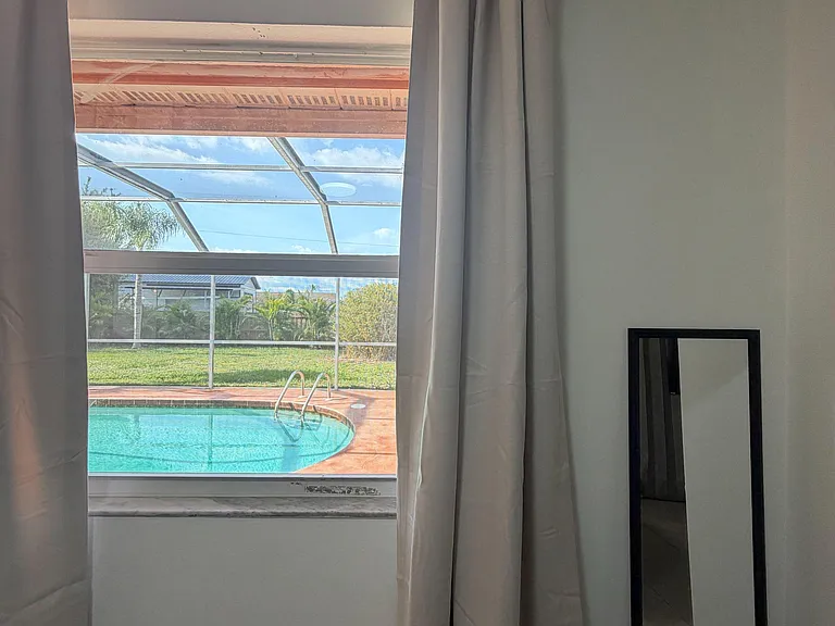 Large window with full-length curtains brings in natural light and offers a view to the screened pool area.
