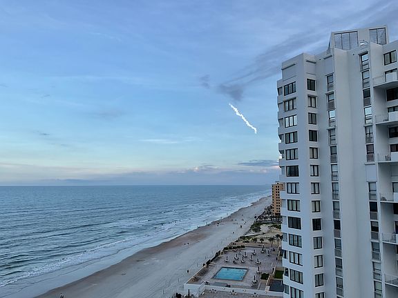 Beach shot looking down coast with a space shot going upward in the distance.